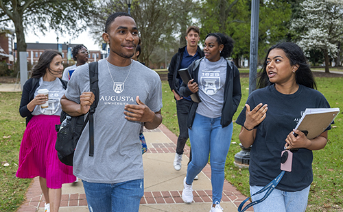 A group of students walk down a sidewalk on a college campus