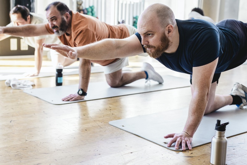 Three men in a yoga class hold bird-dog pose